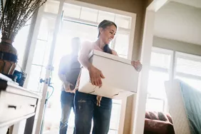 A woman carrying a moving box into a new rented home, illustrating a tenant's personal belongings